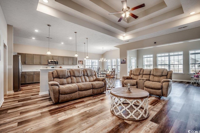 living area with wood finished floors, baseboards, recessed lighting, a raised ceiling, and ceiling fan with notable chandelier