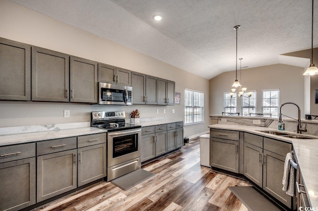 kitchen featuring a notable chandelier, light wood-style flooring, a sink, stainless steel appliances, and lofted ceiling