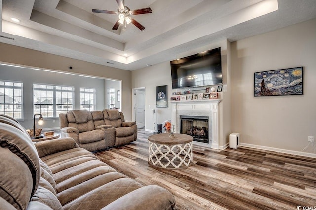 living area with baseboards, ceiling fan, a premium fireplace, wood finished floors, and a raised ceiling