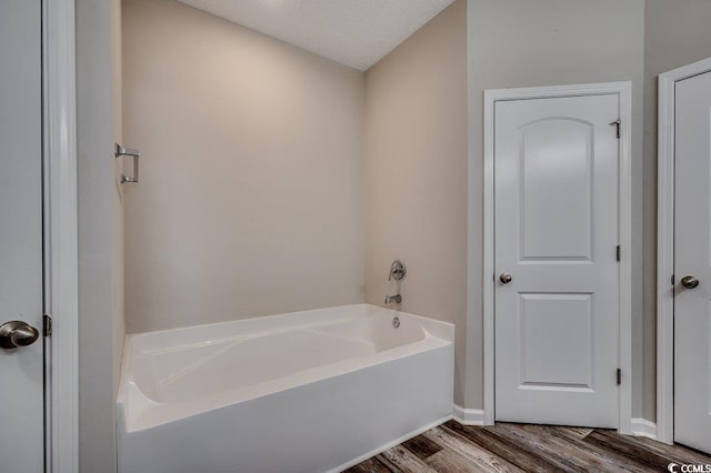 bathroom with a bath, wood finished floors, and a textured ceiling