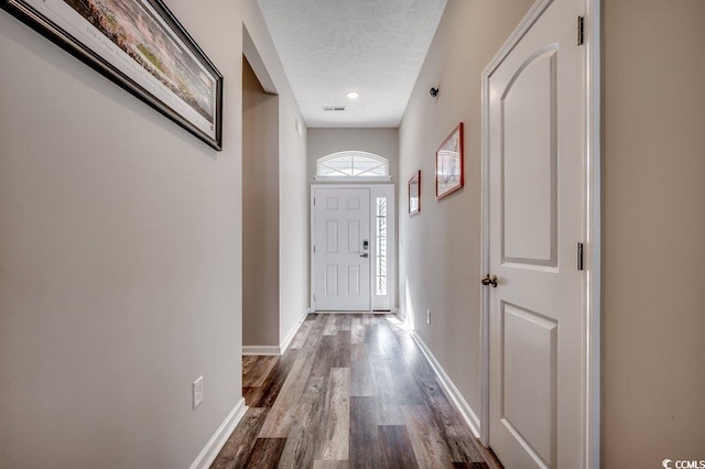 doorway featuring baseboards, a textured ceiling, and dark wood-type flooring