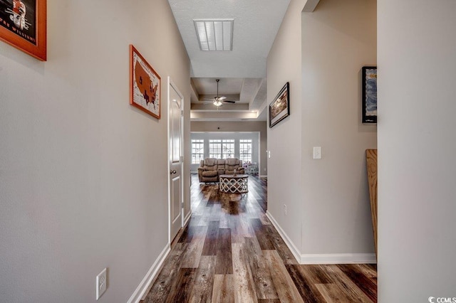 corridor featuring a raised ceiling, baseboards, dark wood-style flooring, and visible vents