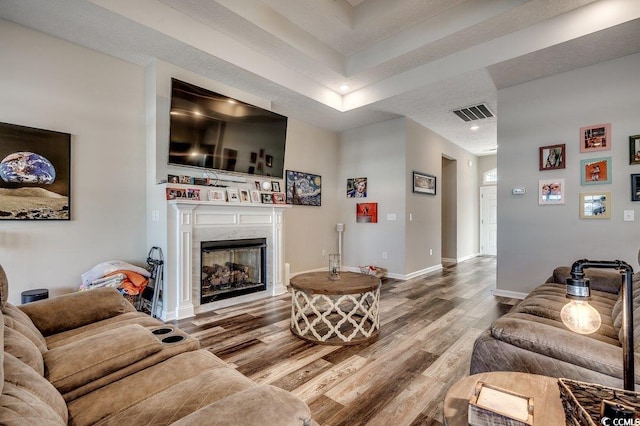 living room with a premium fireplace, visible vents, baseboards, and wood finished floors