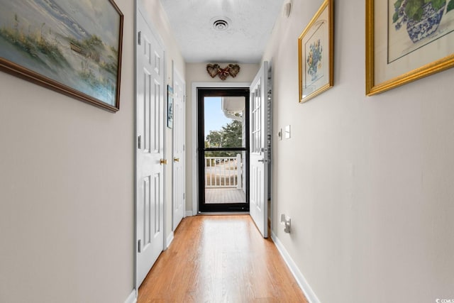 doorway featuring visible vents, baseboards, a textured ceiling, and light wood finished floors