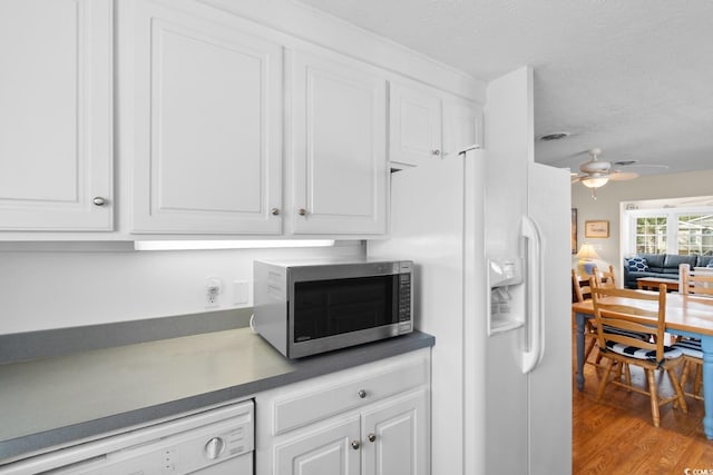 kitchen featuring white appliances, dark countertops, wood finished floors, and white cabinets