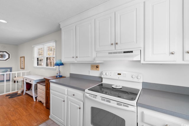 kitchen with white range with electric cooktop, dark countertops, white cabinets, and under cabinet range hood