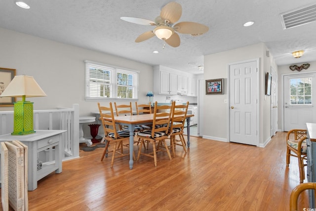 dining space with light wood-type flooring, visible vents, a textured ceiling, and recessed lighting