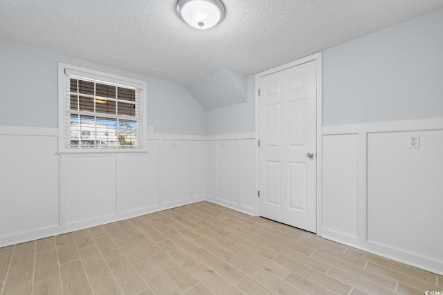 interior space featuring a wainscoted wall, light wood-style flooring, and a textured ceiling