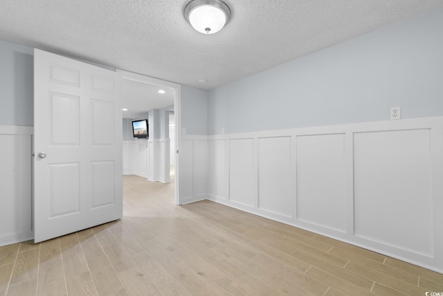 spare room with a decorative wall, light wood-style flooring, and a textured ceiling