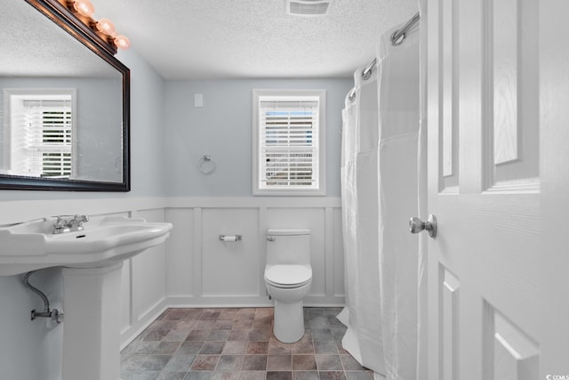 full bath with a healthy amount of sunlight, visible vents, a textured ceiling, and wainscoting