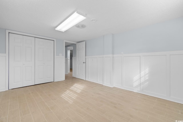 unfurnished bedroom featuring light wood-type flooring, a wainscoted wall, a closet, and a textured ceiling