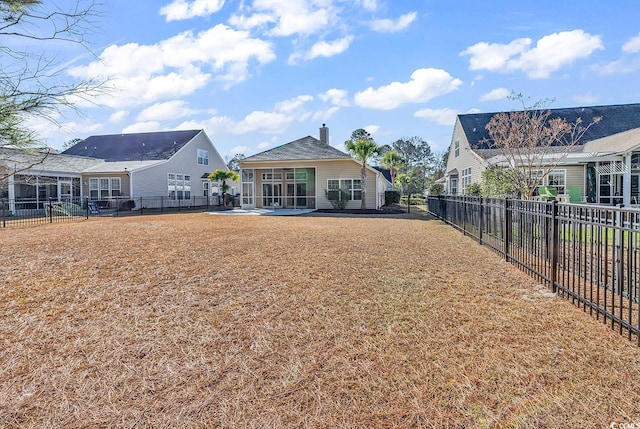 rear view of property featuring a sunroom, a fenced backyard, a yard, and a chimney