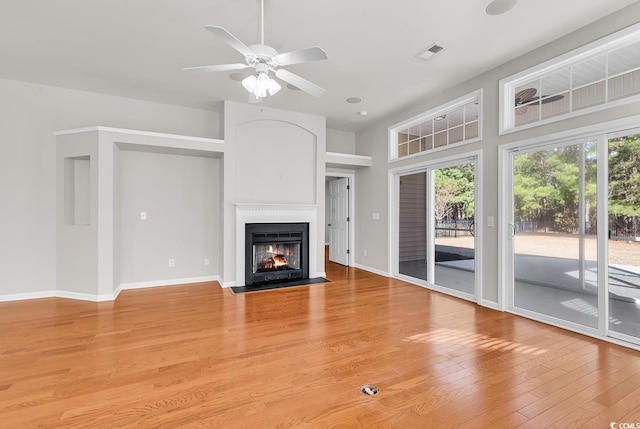 unfurnished living room with visible vents, light wood-style flooring, a fireplace with flush hearth, a ceiling fan, and baseboards