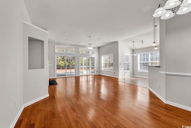 unfurnished living room with wood-type flooring, baseboards, and ceiling fan with notable chandelier