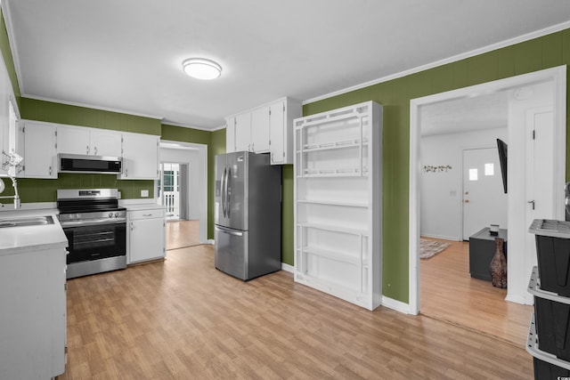 kitchen featuring crown molding, light countertops, light wood-style flooring, appliances with stainless steel finishes, and white cabinetry