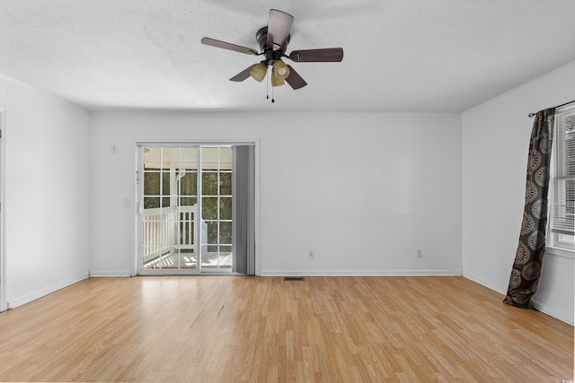 empty room featuring baseboards, light wood-style flooring, visible vents, and a textured ceiling