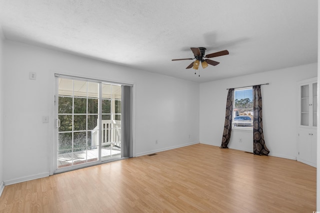 spare room with light wood finished floors, baseboards, visible vents, a ceiling fan, and a textured ceiling