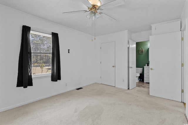 unfurnished bedroom featuring light colored carpet, visible vents, ensuite bathroom, a ceiling fan, and baseboards