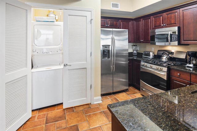 100 N Beach Blvd Unit 1917, North Myrtle Beach, SC 29582 - kitchen with appliances with stainless steel finishes, stacked washer / drying machine, reddish brown cabinets, dark stone counters, and baseboards