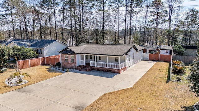 ranch-style house featuring a porch, fence private yard, a shingled roof, brick siding, and driveway