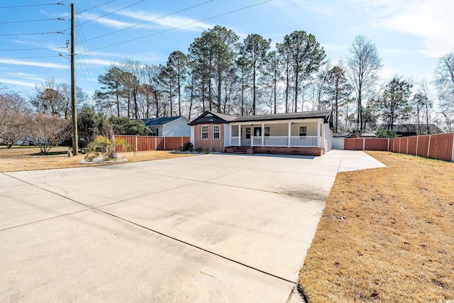 ranch-style house featuring brick siding, covered porch, concrete driveway, a front yard, and fence