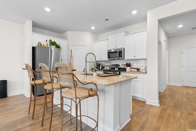 kitchen featuring appliances with stainless steel finishes, white cabinetry, visible vents, and an island with sink