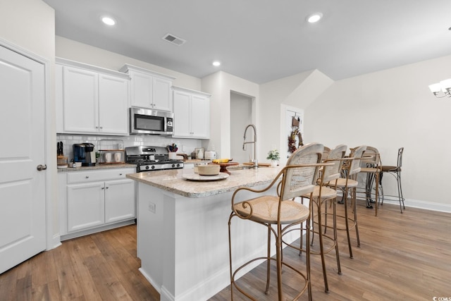 kitchen featuring backsplash, appliances with stainless steel finishes, white cabinetry, an island with sink, and light wood-type flooring