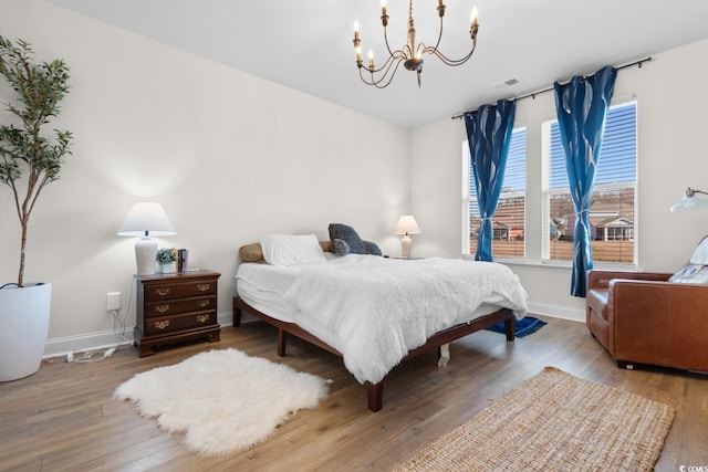 bedroom featuring a chandelier, visible vents, baseboards, and wood finished floors