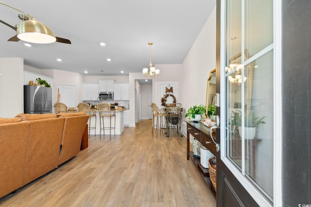 kitchen featuring light wood finished floors, white cabinets, decorative light fixtures, stainless steel appliances, and a kitchen bar