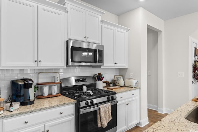 kitchen with appliances with stainless steel finishes, tasteful backsplash, white cabinets, and light stone countertops