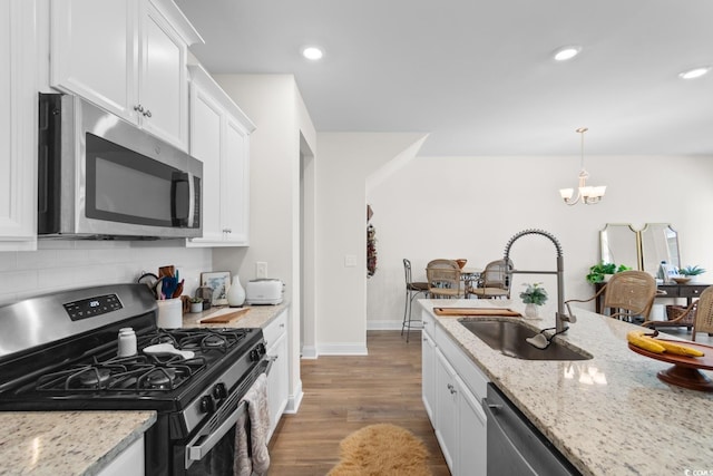 kitchen with light stone counters, a sink, white cabinets, appliances with stainless steel finishes, and pendant lighting