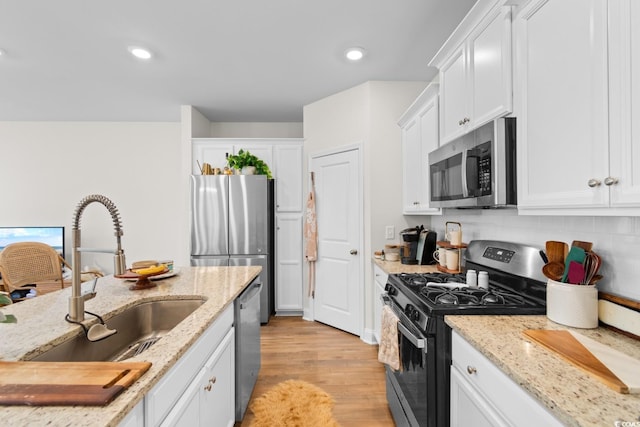 kitchen with stainless steel appliances, white cabinetry, a sink, and light stone countertops