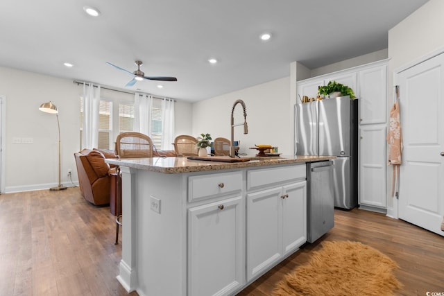 kitchen featuring appliances with stainless steel finishes, white cabinets, a kitchen island with sink, and wood finished floors