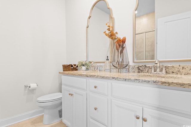 full bath featuring double vanity, toilet, a sink, tiled shower, and baseboards