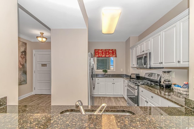 kitchen with light wood finished floors, white cabinets, dark stone counters, stainless steel appliances, and a sink