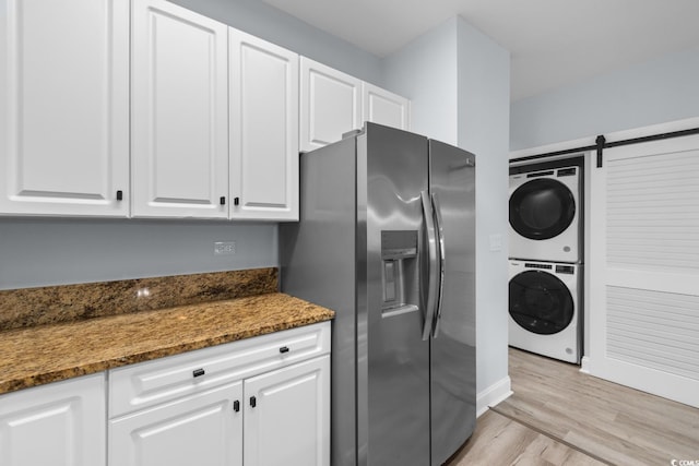 kitchen with stacked washer and dryer, white cabinetry, light wood finished floors, dark stone countertops, and stainless steel fridge