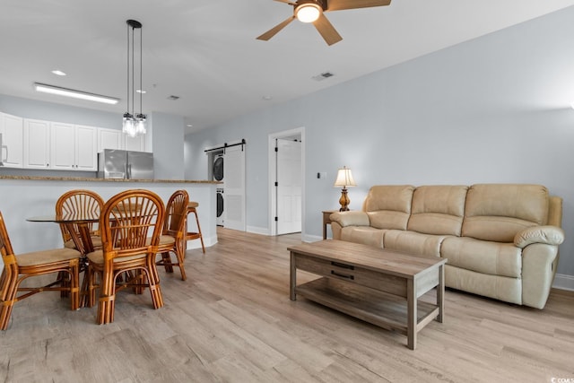 living area featuring stacked washer / drying machine, visible vents, a barn door, ceiling fan, and light wood-type flooring