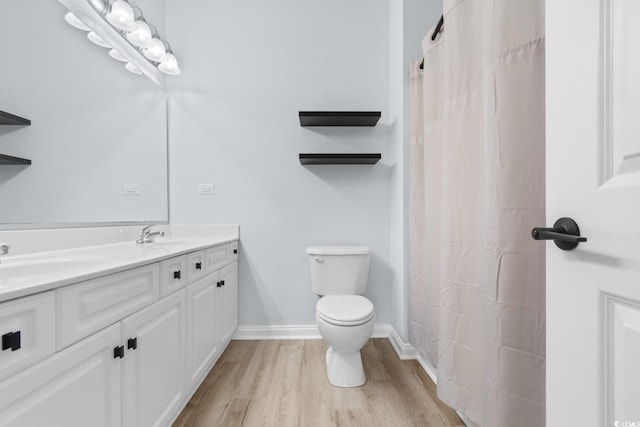 bathroom featuring double vanity, baseboards, toilet, wood finished floors, and a sink