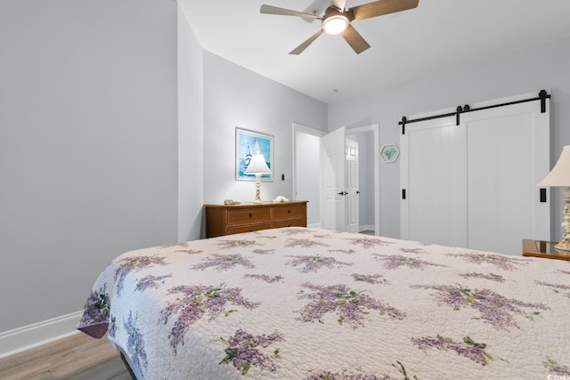 bedroom with a barn door, baseboards, ceiling fan, light wood-style floors, and a closet