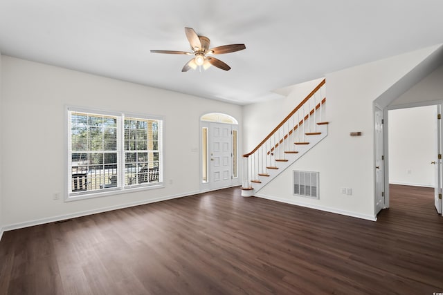 unfurnished living room with dark wood finished floors, visible vents, a ceiling fan, baseboards, and stairs