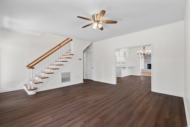 unfurnished living room with stairway, ceiling fan with notable chandelier, baseboards, dark wood-type flooring, and visible vents