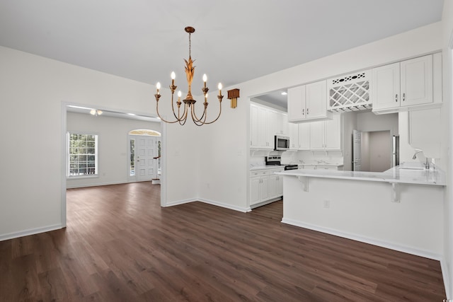 kitchen with white cabinets, stainless steel appliances, dark wood-type flooring, a peninsula, and a notable chandelier