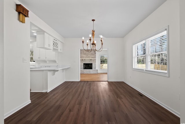 unfurnished living room with dark wood-style floors, baseboards, a brick fireplace, and a chandelier