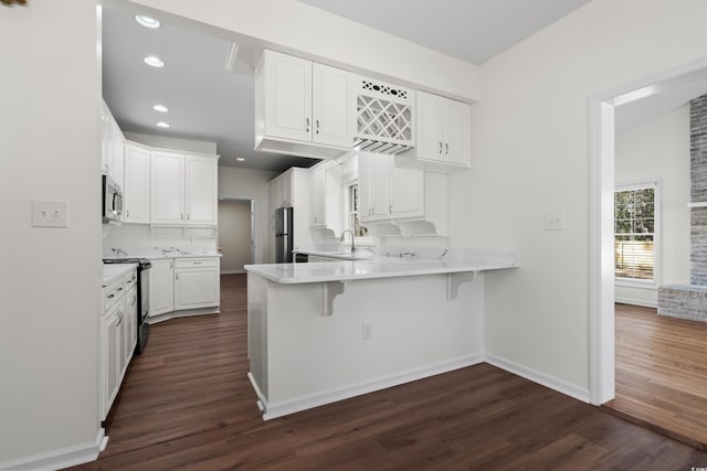 kitchen with dark wood finished floors, appliances with stainless steel finishes, a breakfast bar, a peninsula, and a sink