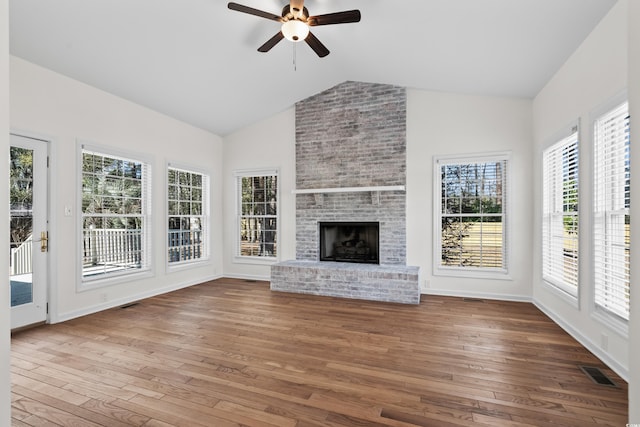 interior space with lofted ceiling, visible vents, a ceiling fan, a brick fireplace, and hardwood / wood-style floors