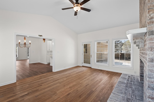 spare room with vaulted ceiling, a fireplace, hardwood / wood-style floors, and ceiling fan with notable chandelier