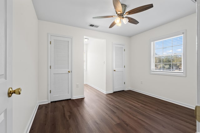 unfurnished bedroom featuring dark wood-style flooring, a ceiling fan, multiple closets, visible vents, and baseboards