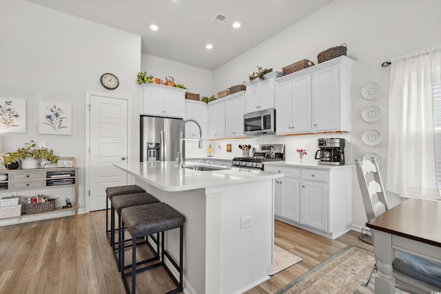 kitchen featuring visible vents, light wood-style flooring, appliances with stainless steel finishes, a kitchen bar, and a sink