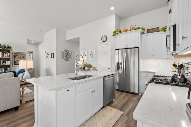 kitchen with appliances with stainless steel finishes, a kitchen island with sink, white cabinets, a sink, and wood finished floors