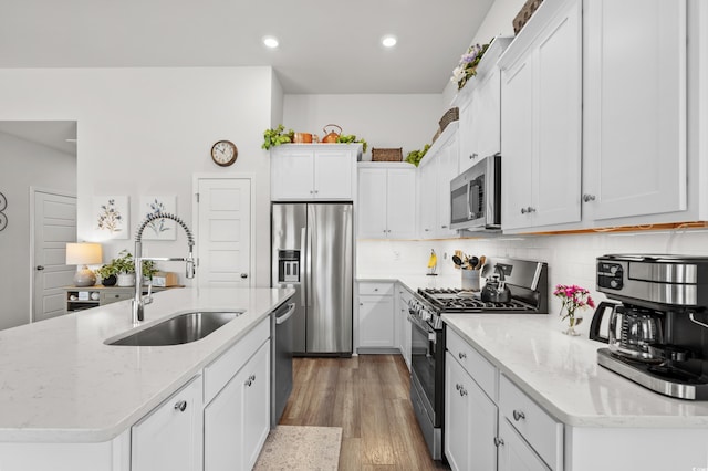 kitchen featuring light wood finished floors, an island with sink, appliances with stainless steel finishes, white cabinetry, and a sink